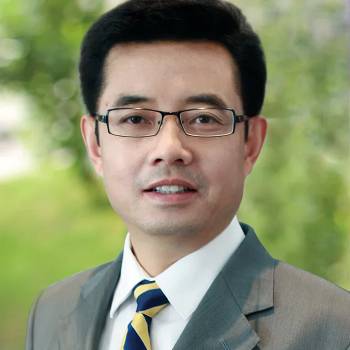 James Jian Ho MD PhD Mayo Fellow vilkintis juodą smokingą ir varlytę, stovi priešais banerį su logotipais, įskaitant Oscars ir HeartDaHeart Foundation, oficiali renginio aplinka, neutralus ir profesionalus įspūdis, matomas tekstas: Oscars HeartDaHeart Foundation UnmaskHeartDisease